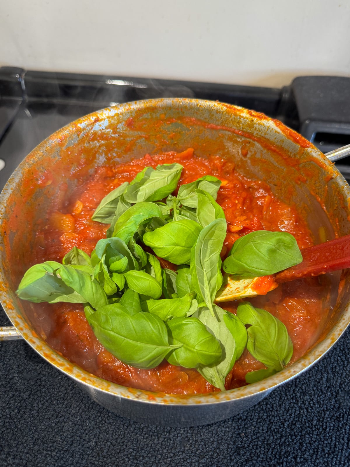 adding fresh basil leaves to sauce to wilt